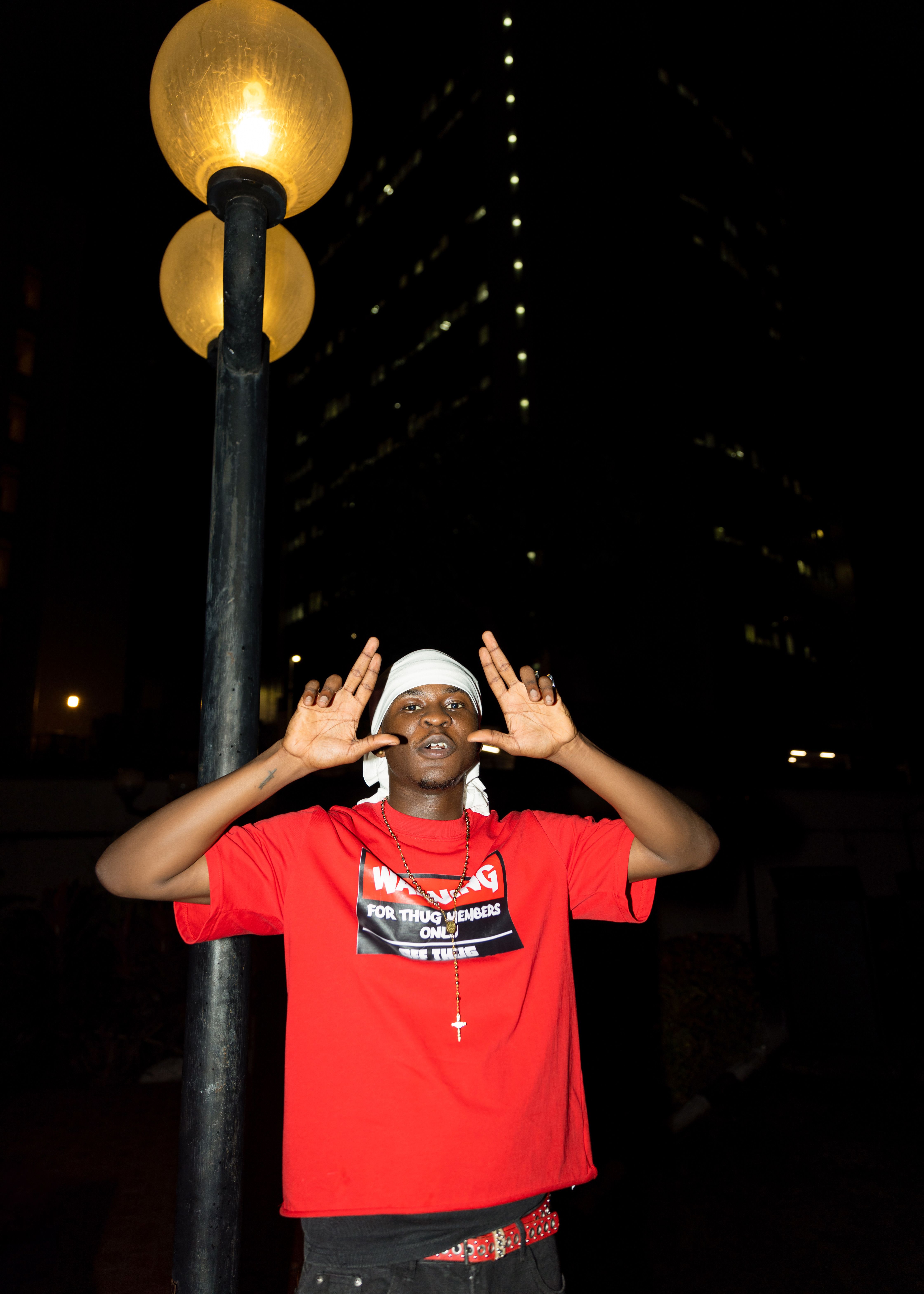 Urban night scene with a young man wearing red under a streetlight.
