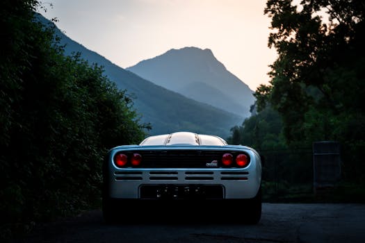 A stunning vintage supercar set against a serene mountain backdrop at sunset.