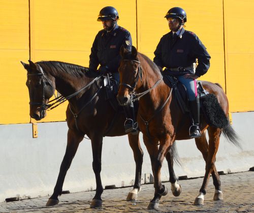 Free Two mounted police officers riding horses beside a yellow building wall. Stock Photo
