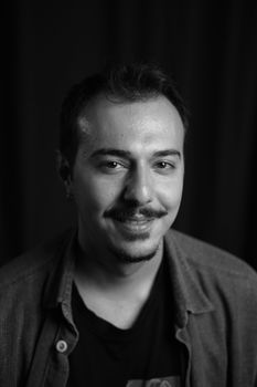 Studio portrait of a smiling man with a beard and mustache, in casual attire.