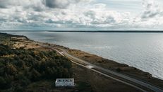 Aerial view of a peaceful coastal road alongside lush greenery and a vast body of water.