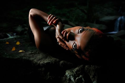 A captivating portrait of a model laying on a rock near a waterfall.