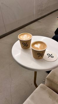 Two latte art coffees in branded paper cups on a sleek round table.