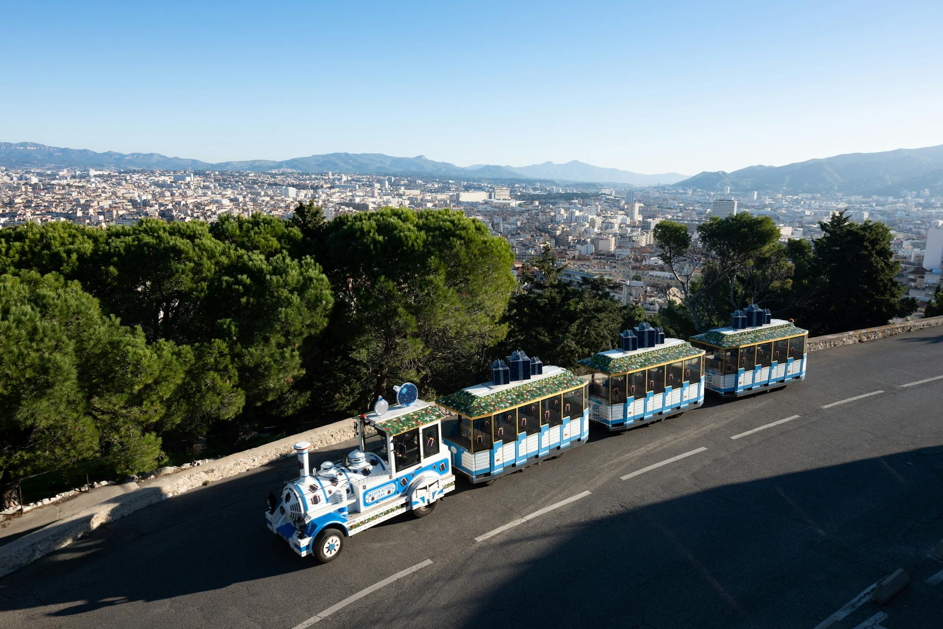 A picturesque tourist train overlooking Marseille cityscape on a sunny day.