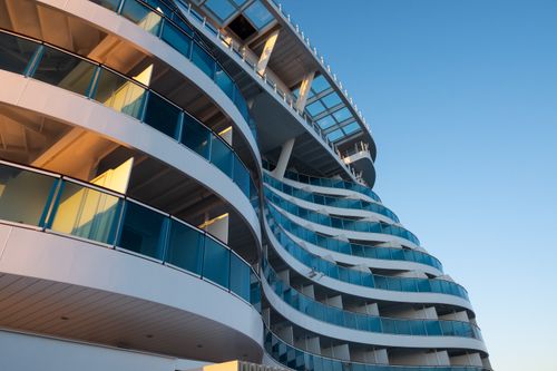 Free Low-angle view of a modern cruise ship with curved balconies and blue glass, under a clear sky. Stock Photo