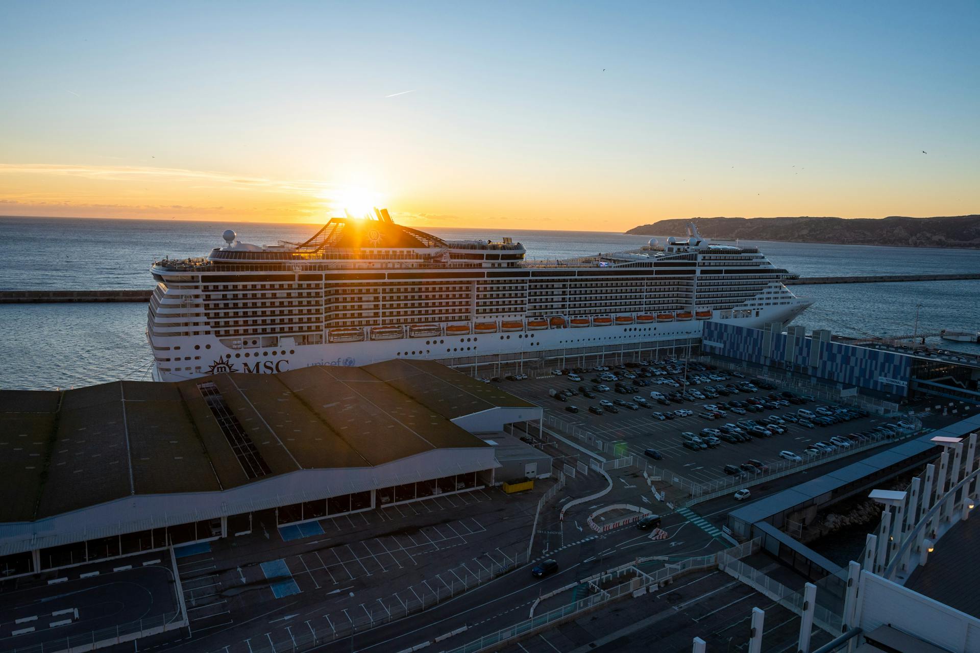 A cruise ship docked at Marseille port during sunset with a clear sky and vibrant colors.