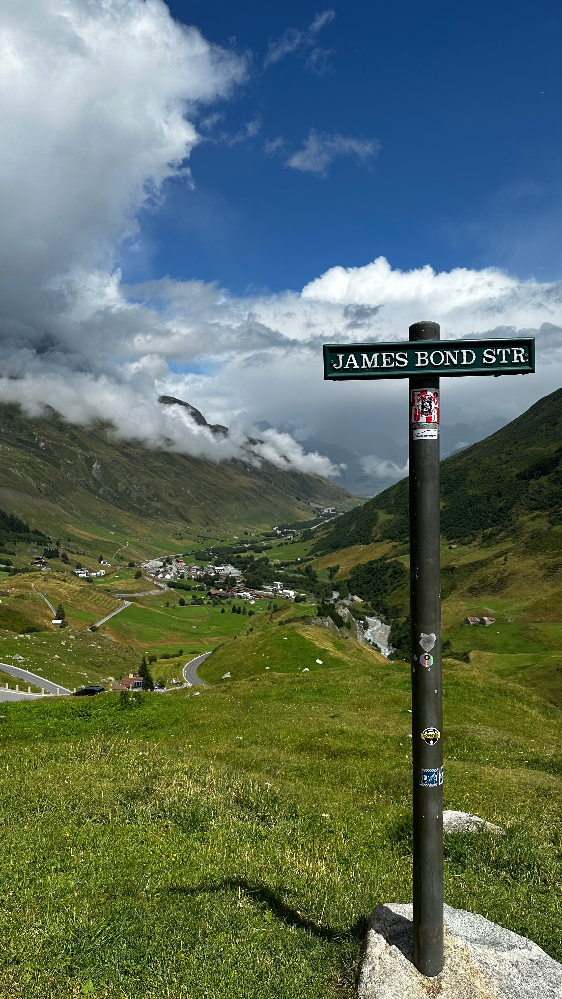 Landscape view in Swiss Alps with a signpost labeled James Bond Street, under a vibrant blue sky.