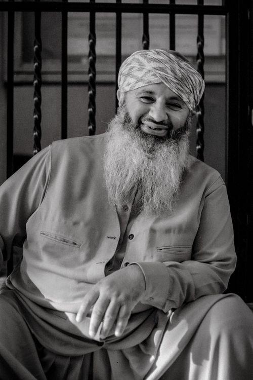 Free Candid black and white portrait of a smiling elderly man with a long beard wearing traditional attire. Stock Photo