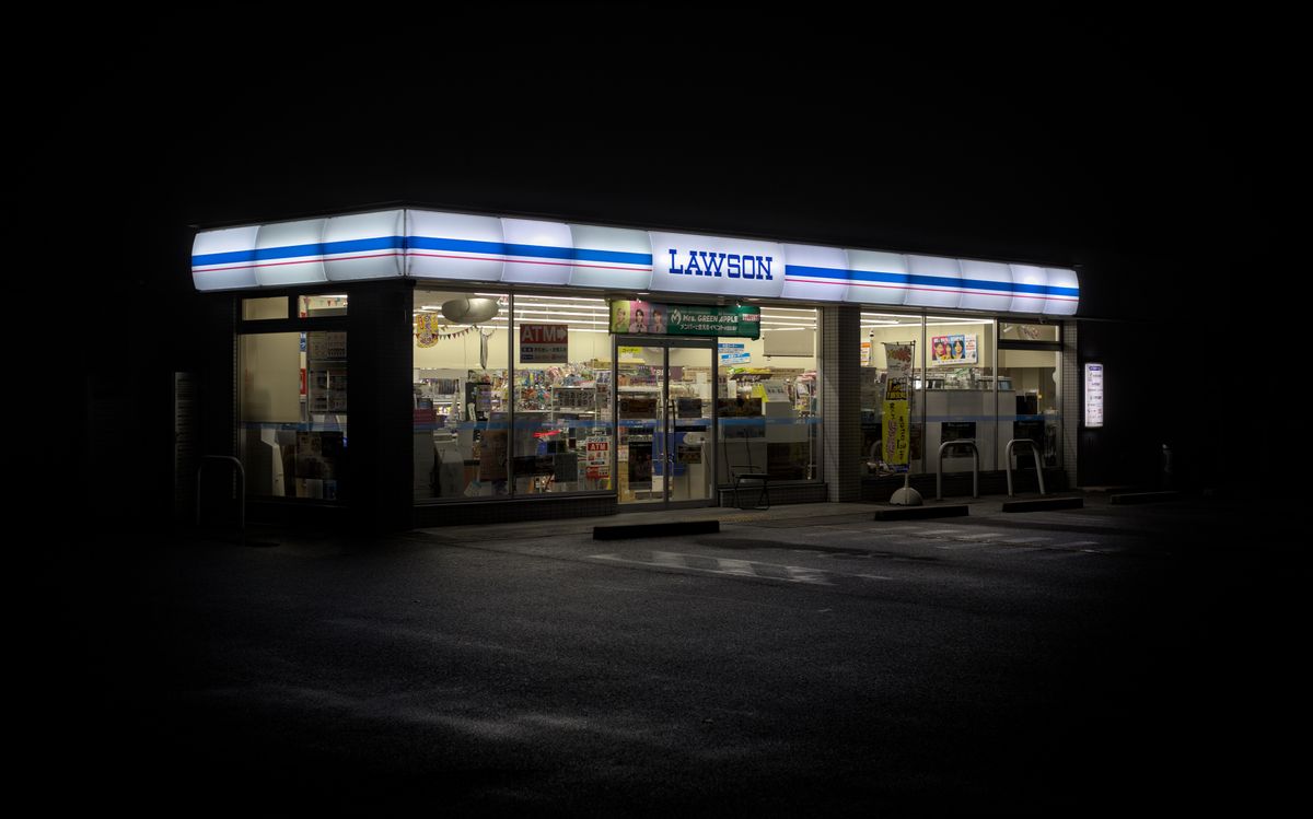 A Lawson convenience store at night, with an ATM sign in the window