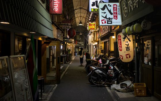 Night view of a vibrant Osaka alley with lanterns, bicycles, and illuminated signboards.
