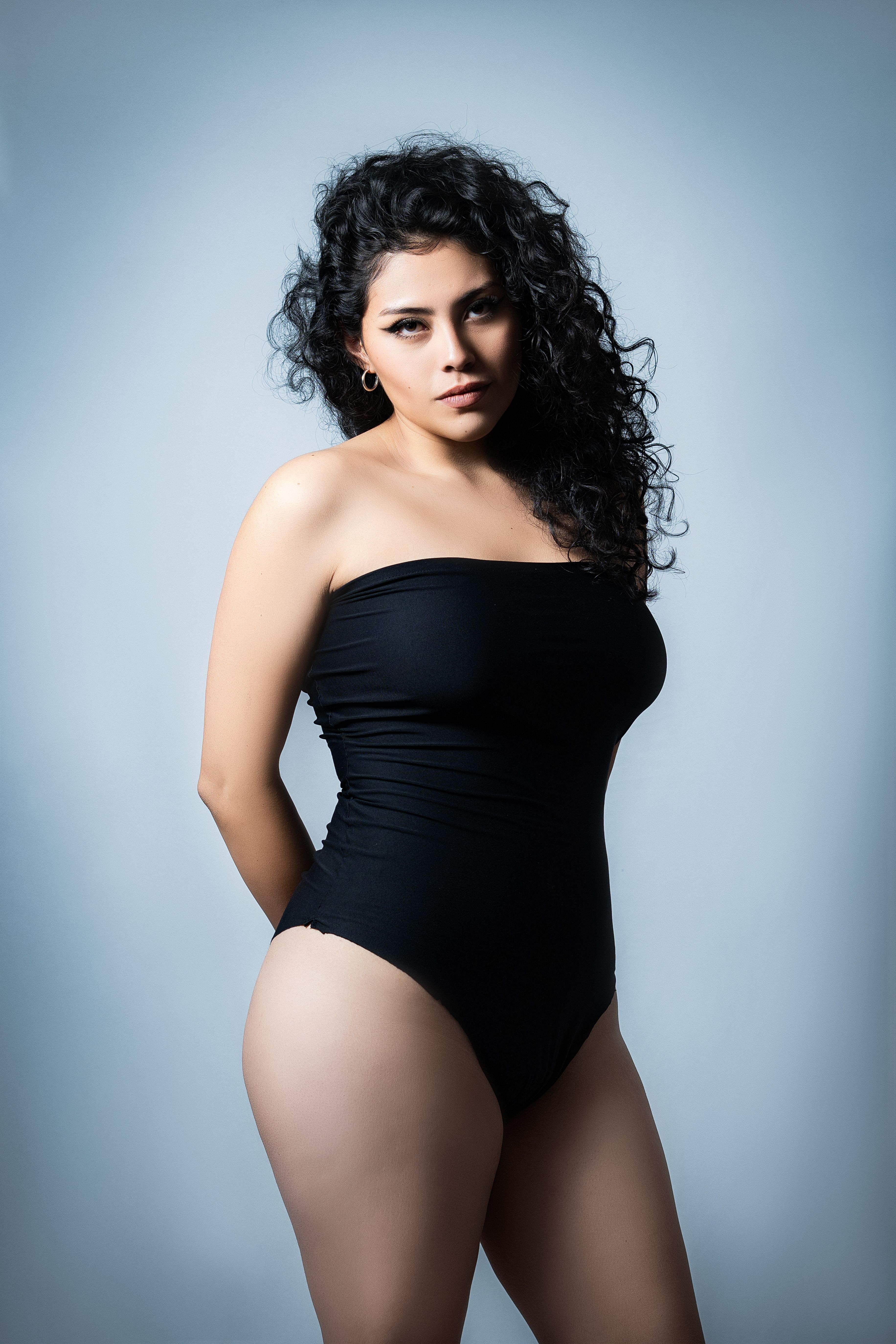 A stylish and confident woman poses elegantly in a black outfit against a neutral background.