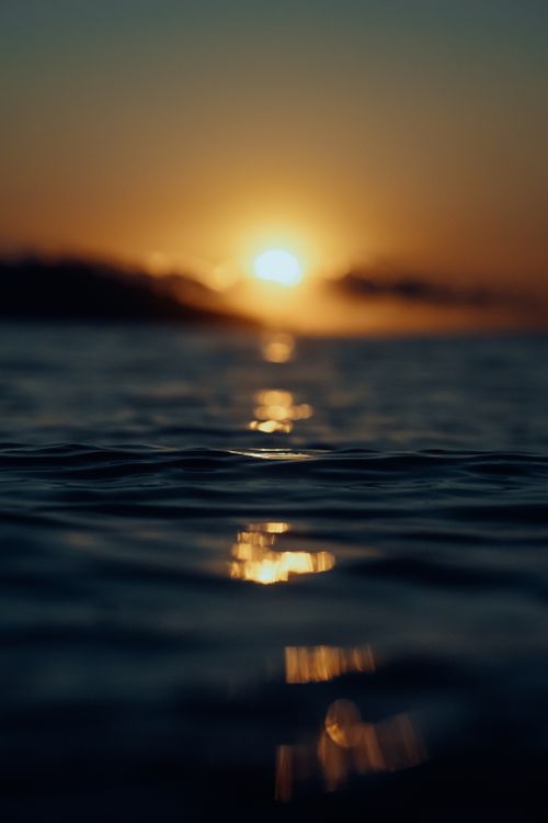 Free A tranquil sunset over the ocean with vibrant reflections on the water surface, capturing the essence of peace. Stock Photo