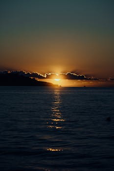 A stunning sunset casting a warm glow over the tranquil ocean, creating a peaceful ambiance.