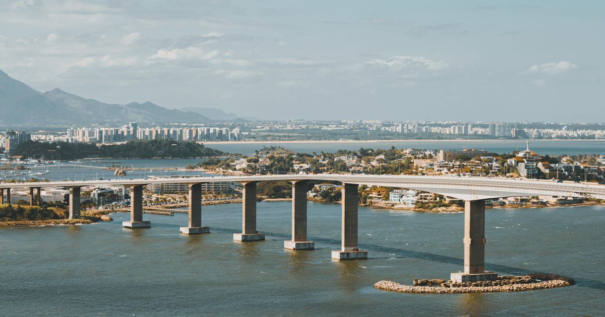 Vista aérea de uma deslumbrante ponte conectando paisagens urbanas, com montanhas ao fundo.