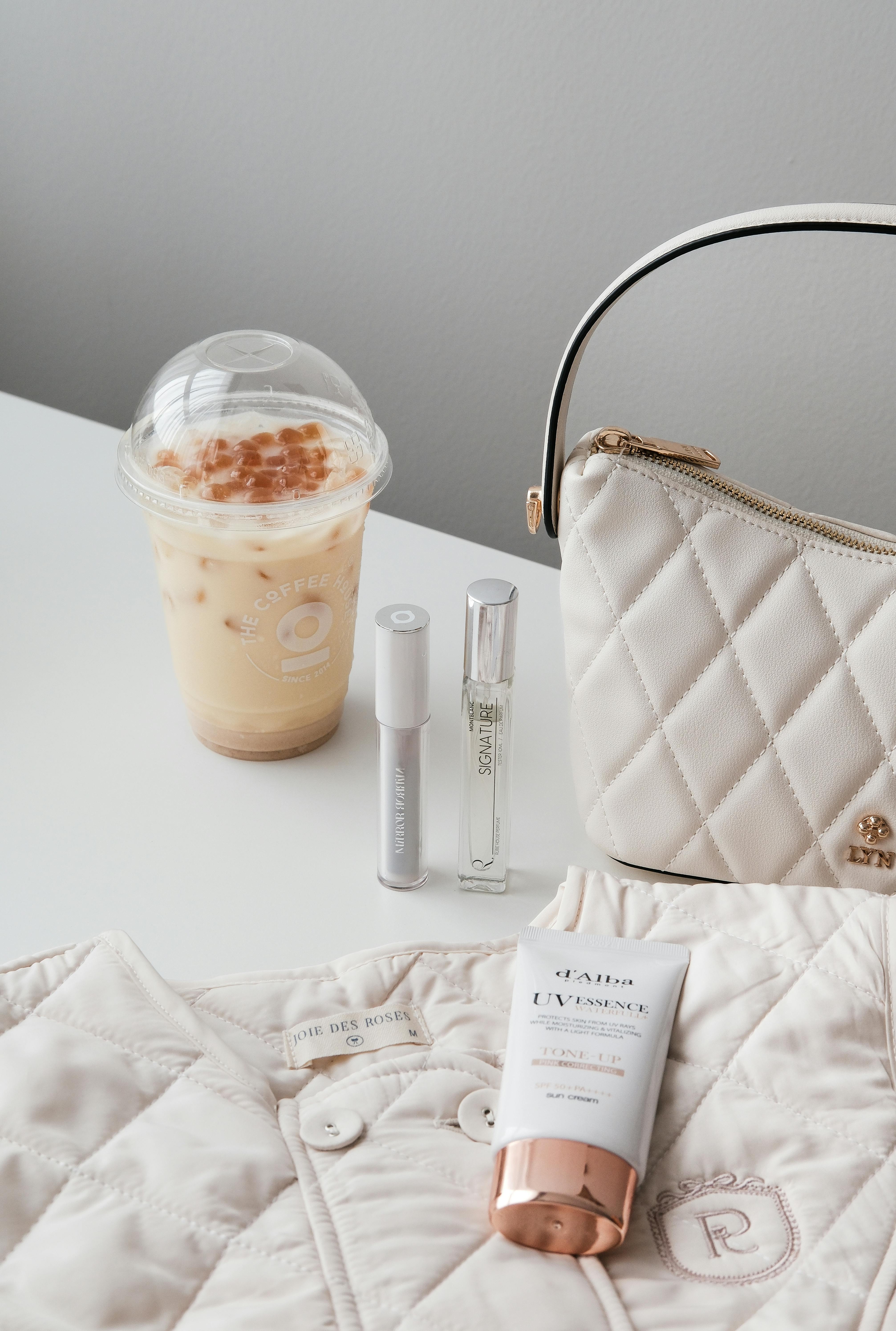 Flat lay of trendy Asian cosmetics, coffee, bag, and clothing on white background.