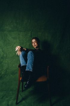 Artistic portrait of a woman seated on a chair in a moody, dark studio setting.