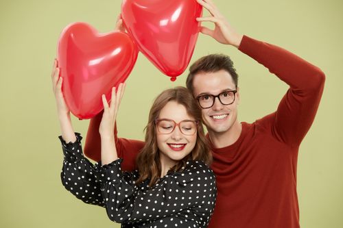 Free A joyful couple with heart balloons and eyeglasses posing against a green background. Stock Photo
