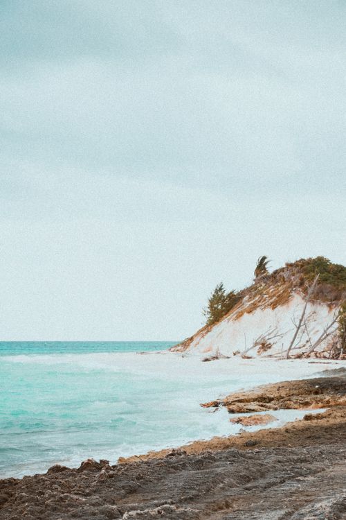 Free A tranquil coastline with rocky cliffs and turquoise ocean waves under a cloudy sky. Stock Photo