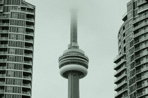 Free CN Tower amidst fog between Toronto's skyscrapers, creating an iconic urban scene. Stock Photo