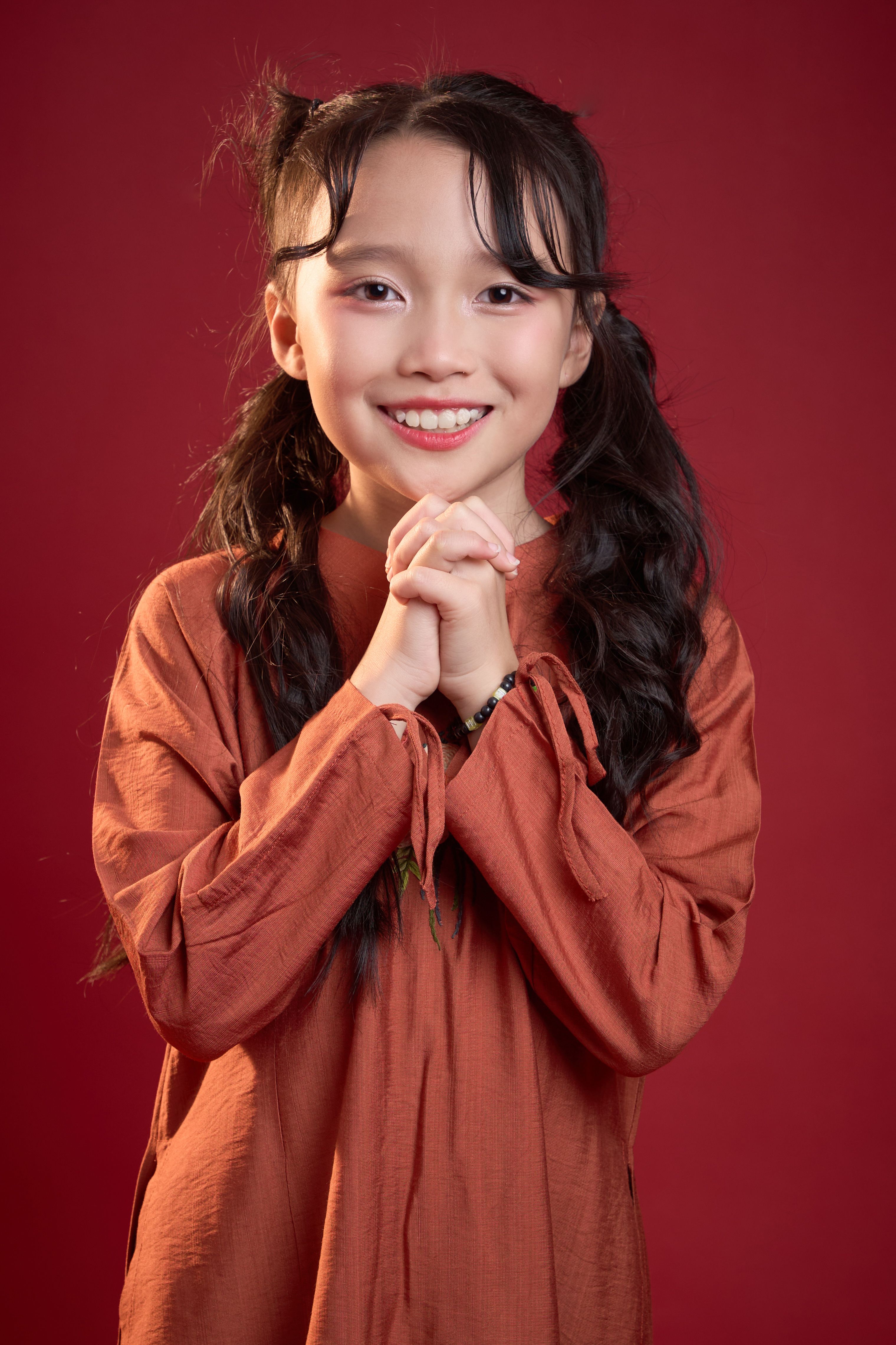 Young Vietnamese girl posing confidently against a rich red backdrop.