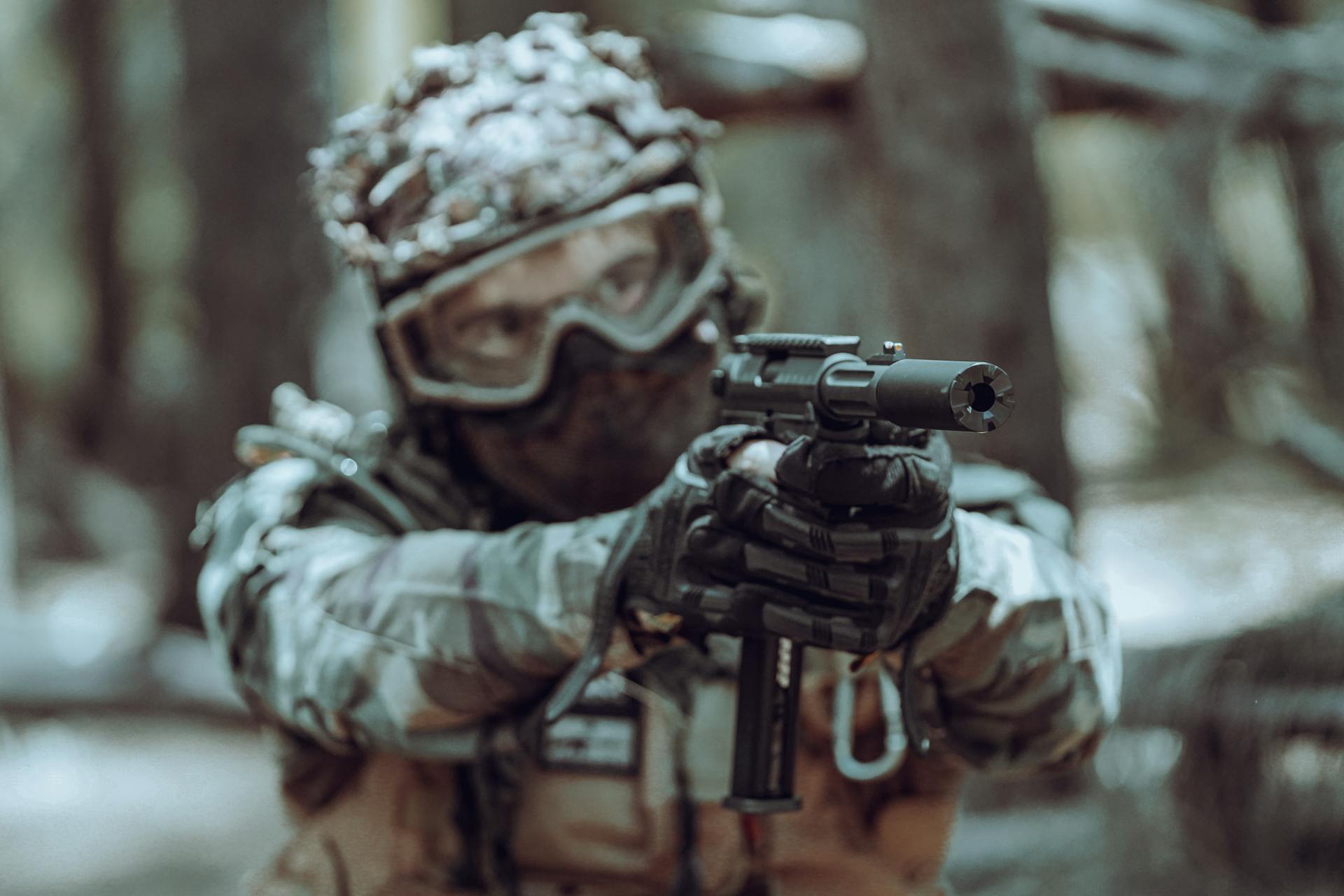 A focused soldier in tactical gear aiming a handgun in a forest setting.