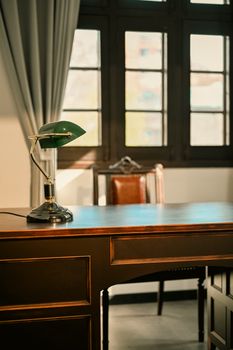 A sunlit study room with a vintage wooden desk and classic desk lamp.