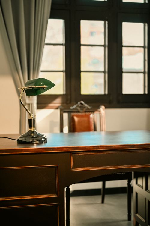 Free A sunlit study room with a vintage wooden desk and classic desk lamp. Stock Photo