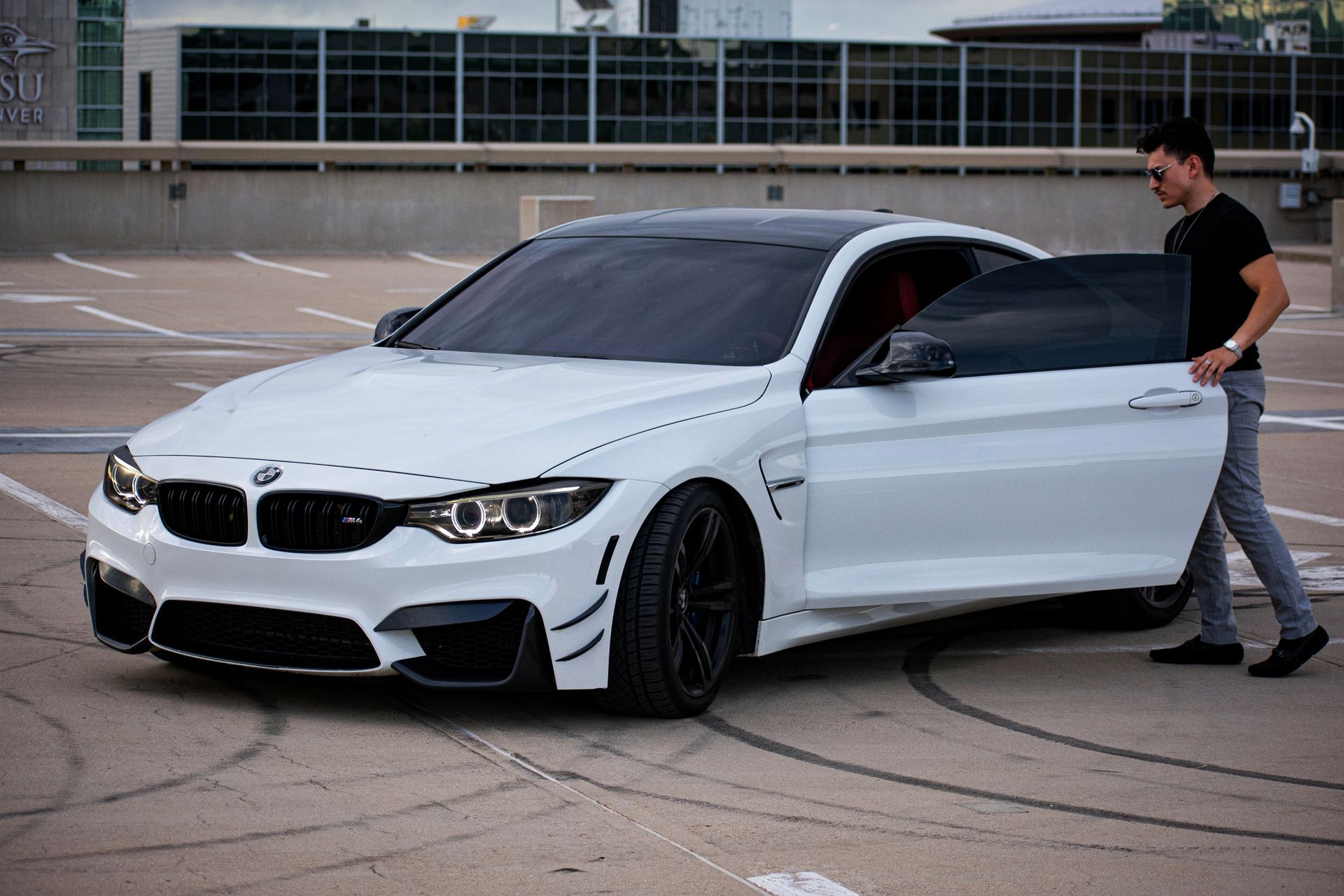 Man exiting luxury white sports car in urban rooftop parking area.