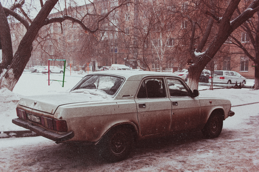 Retro car parked in a snowy urban area, evoking nostalgia and cold winter vibe.