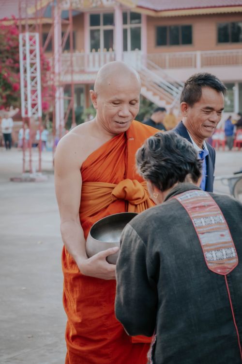 Free An elderly person offers alms to a Buddhist monk in a traditional ceremony outdoors. Stock Photo