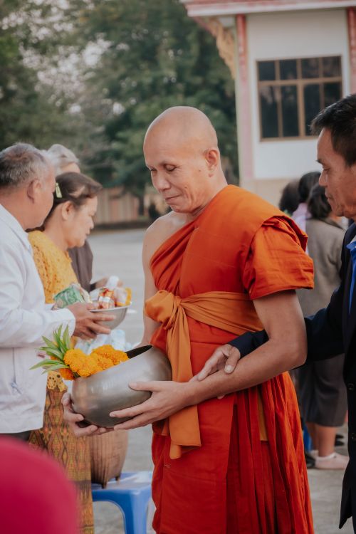 Free A Buddhist monk in orange robe receives offerings during a traditional ceremony outdoors. Stock Photo