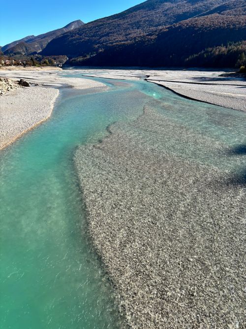 Free A breathtaking turquoise river flows through a serene mountain valley under clear blue sky. Stock Photo