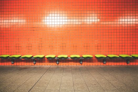 A row of green seats against a vibrant orange tiled wall in a contemporary indoor setting.