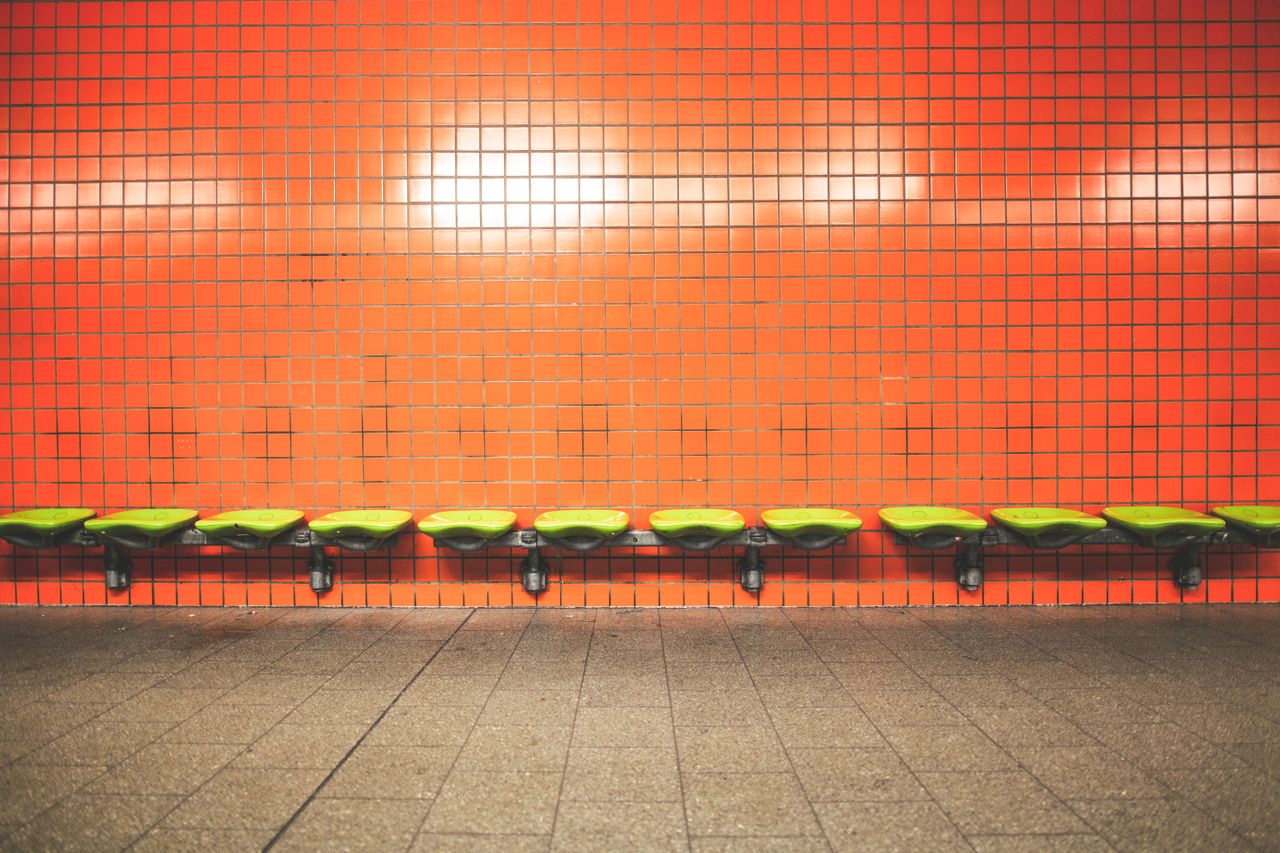 a row of green seats against a vibrant orange tiled wall in a contempo