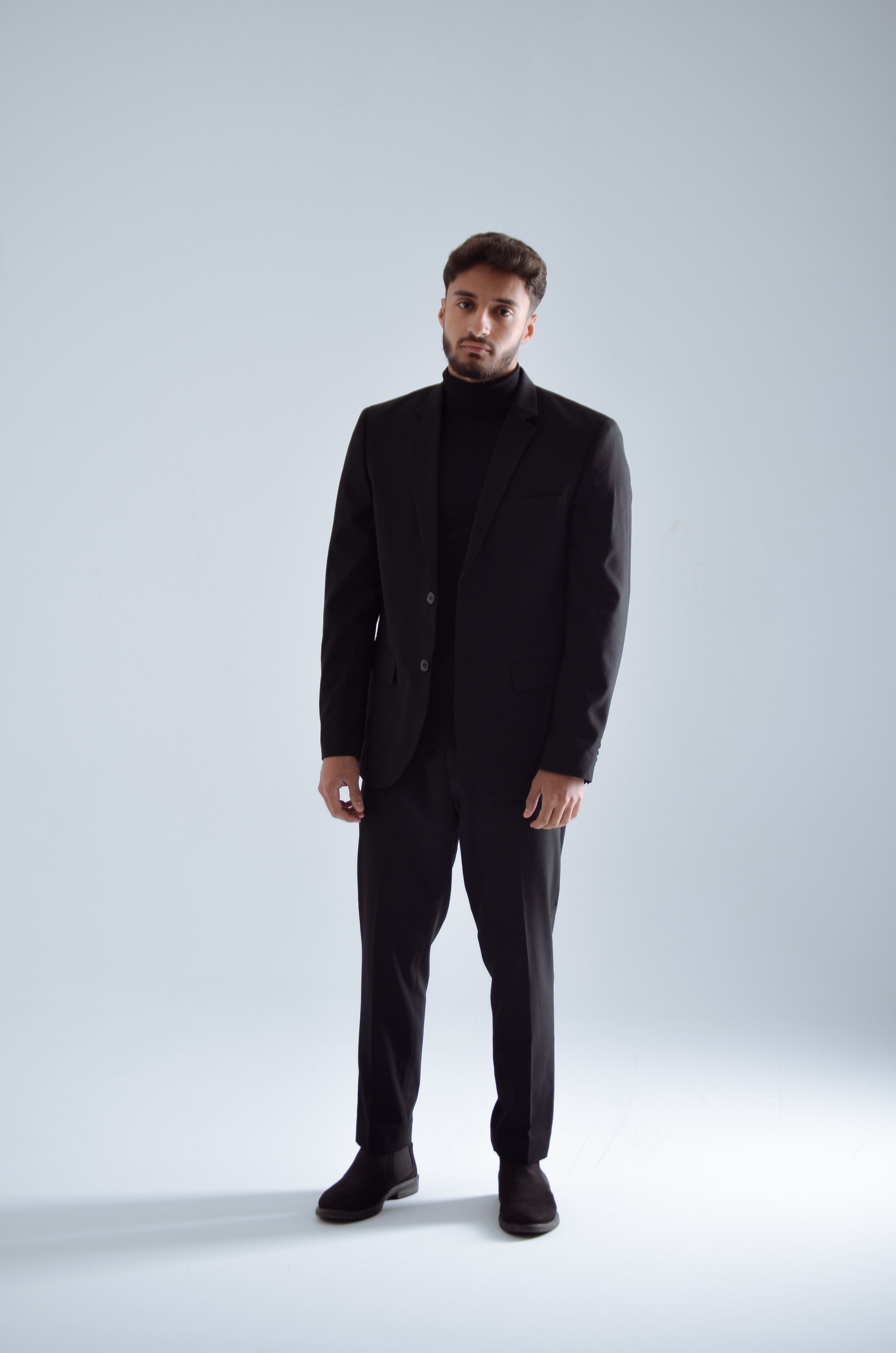 grátis Jovem elegante em um elegante terno preto posando em um ambiente interno com um fundo minimalista. Foto profissional