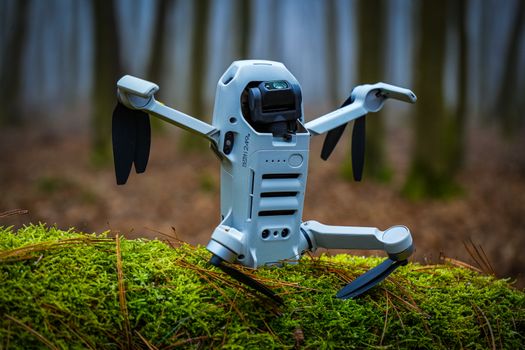 A sleek drone perched on moss, ready for aerial adventures in a forest.