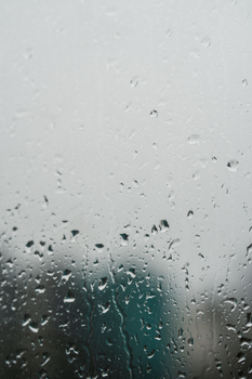 Raindrops on a window create a textured view of a blurred cityscape, evoking a moody atmosphere.