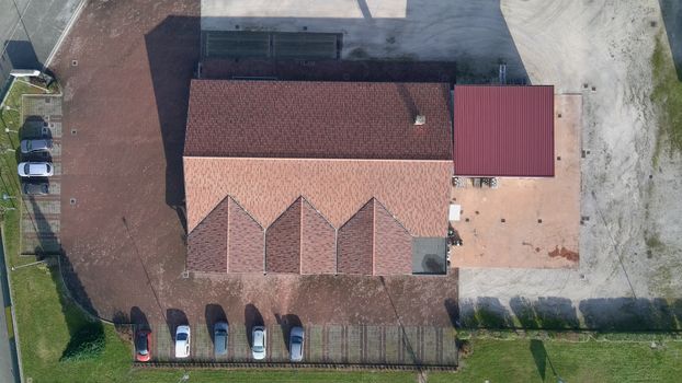 Aerial view of a building with a red roof and parked cars, highlighting architectural design.