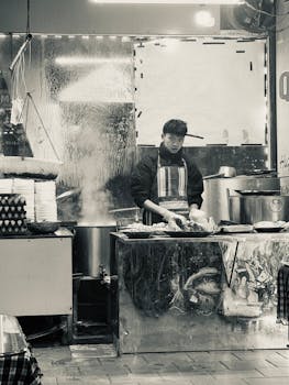 Monochrome image of a vendor cooking at a bustling street market stall.