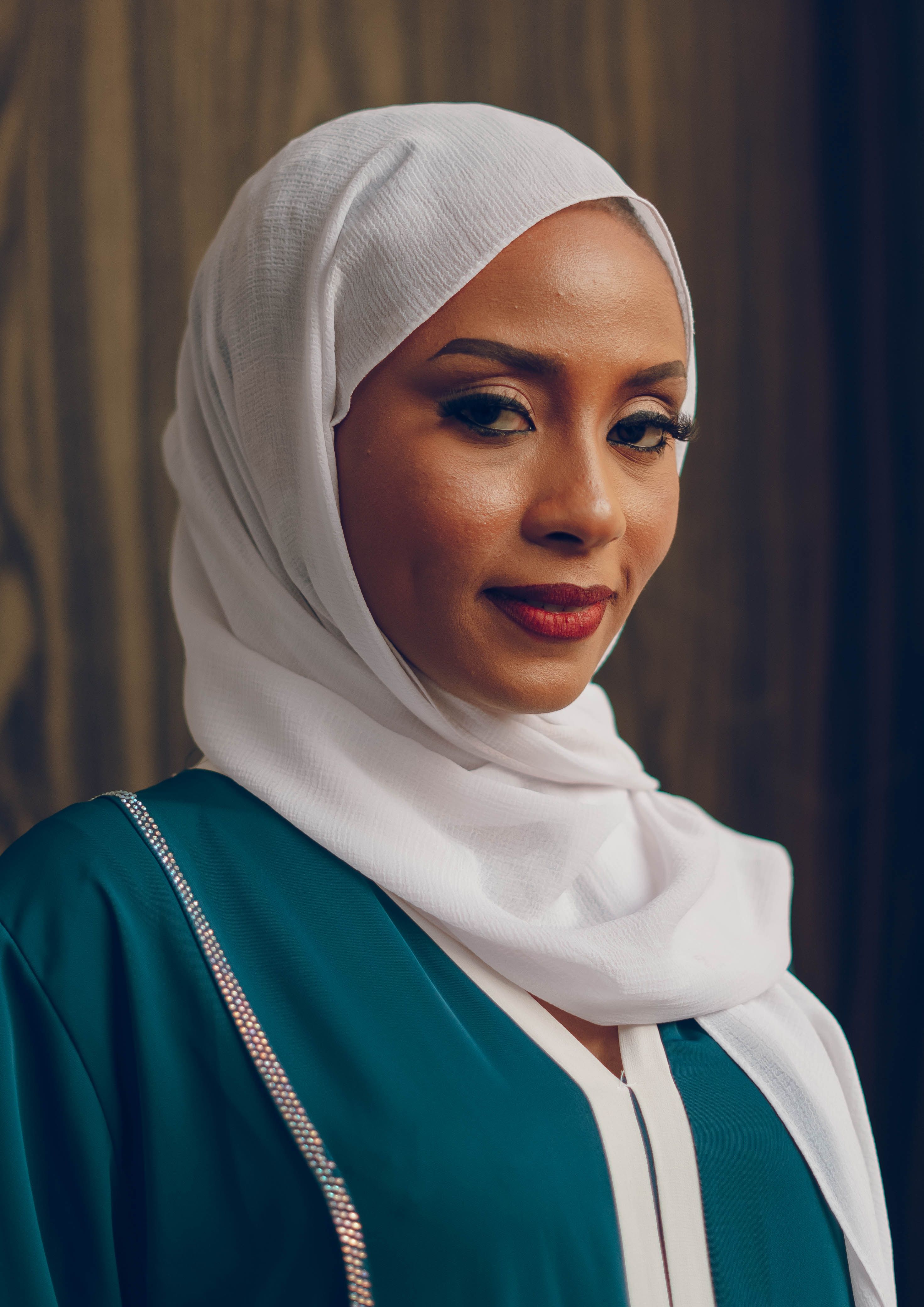 Close-up portrait of a woman wearing a white hijab and traditional dress, indoors.