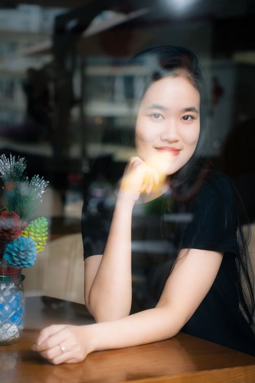 Free Portrait of a young woman smiling through a cafe window with festive decor. Stock Photo