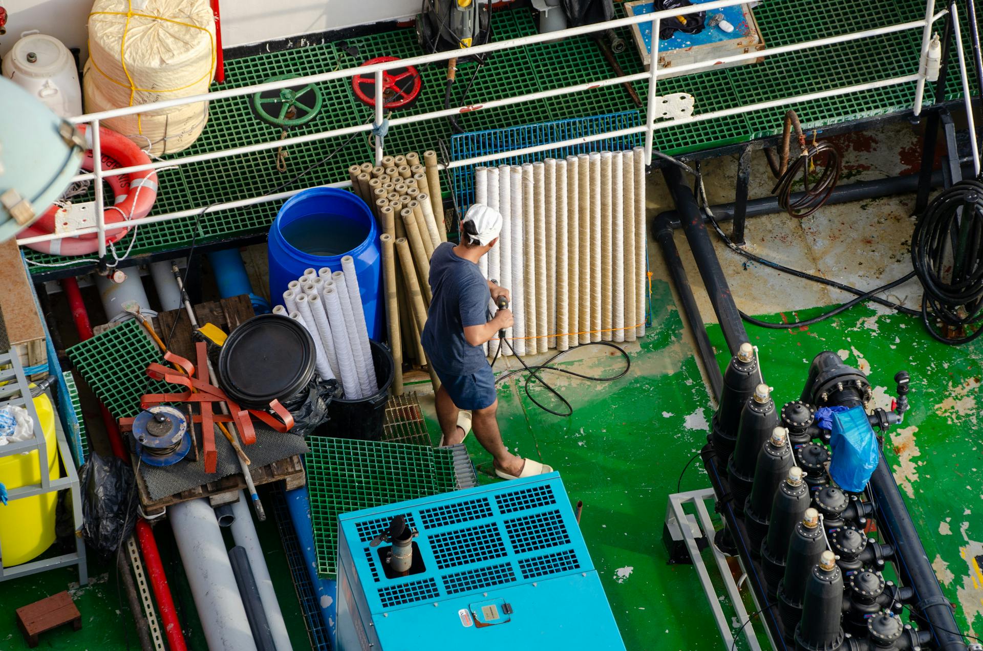 Aerial view of a worker on a ship deck managing industrial equipment and pipes.