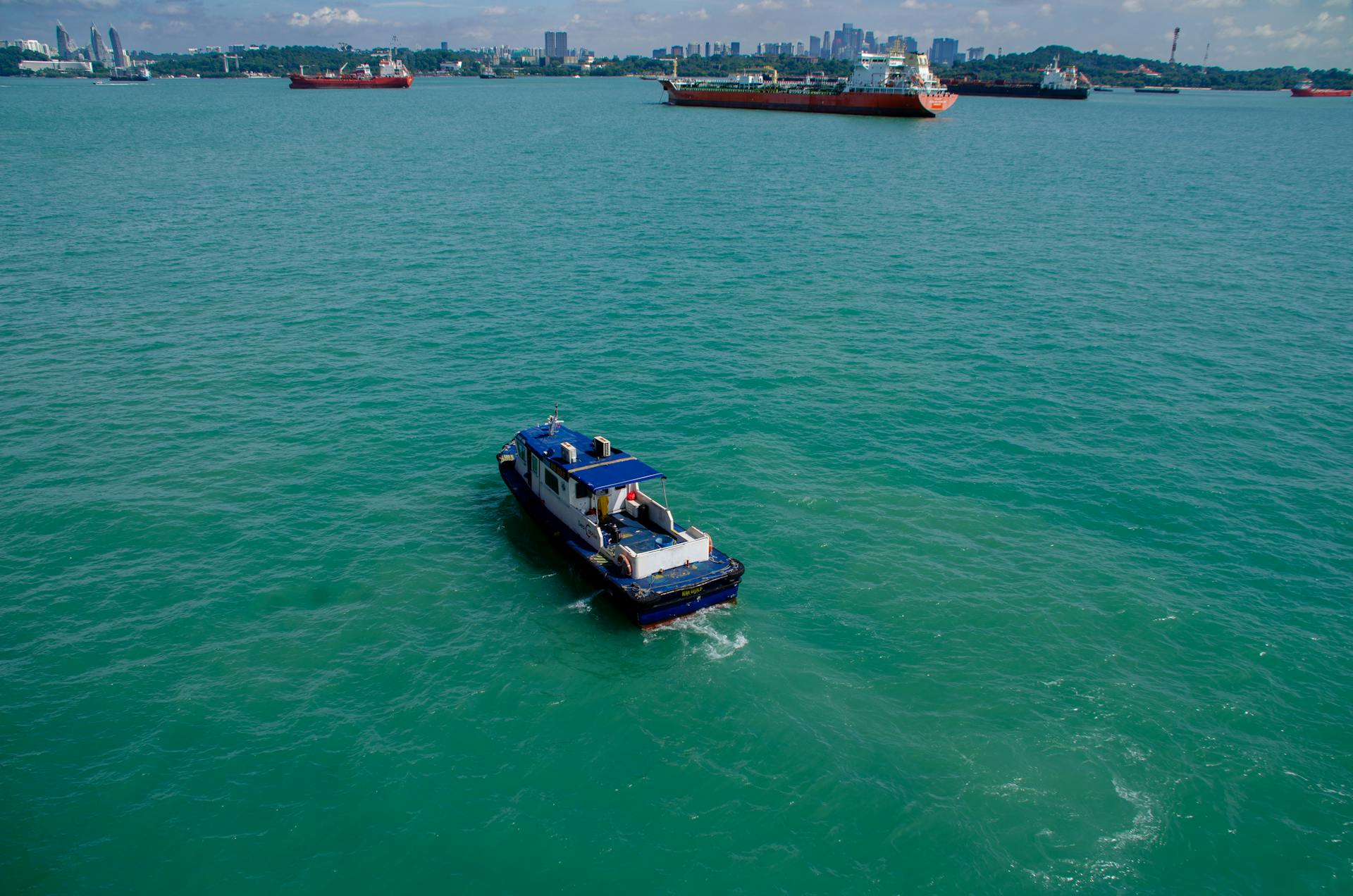 A lone boat navigates through a bustling shipping channel on a clear day.