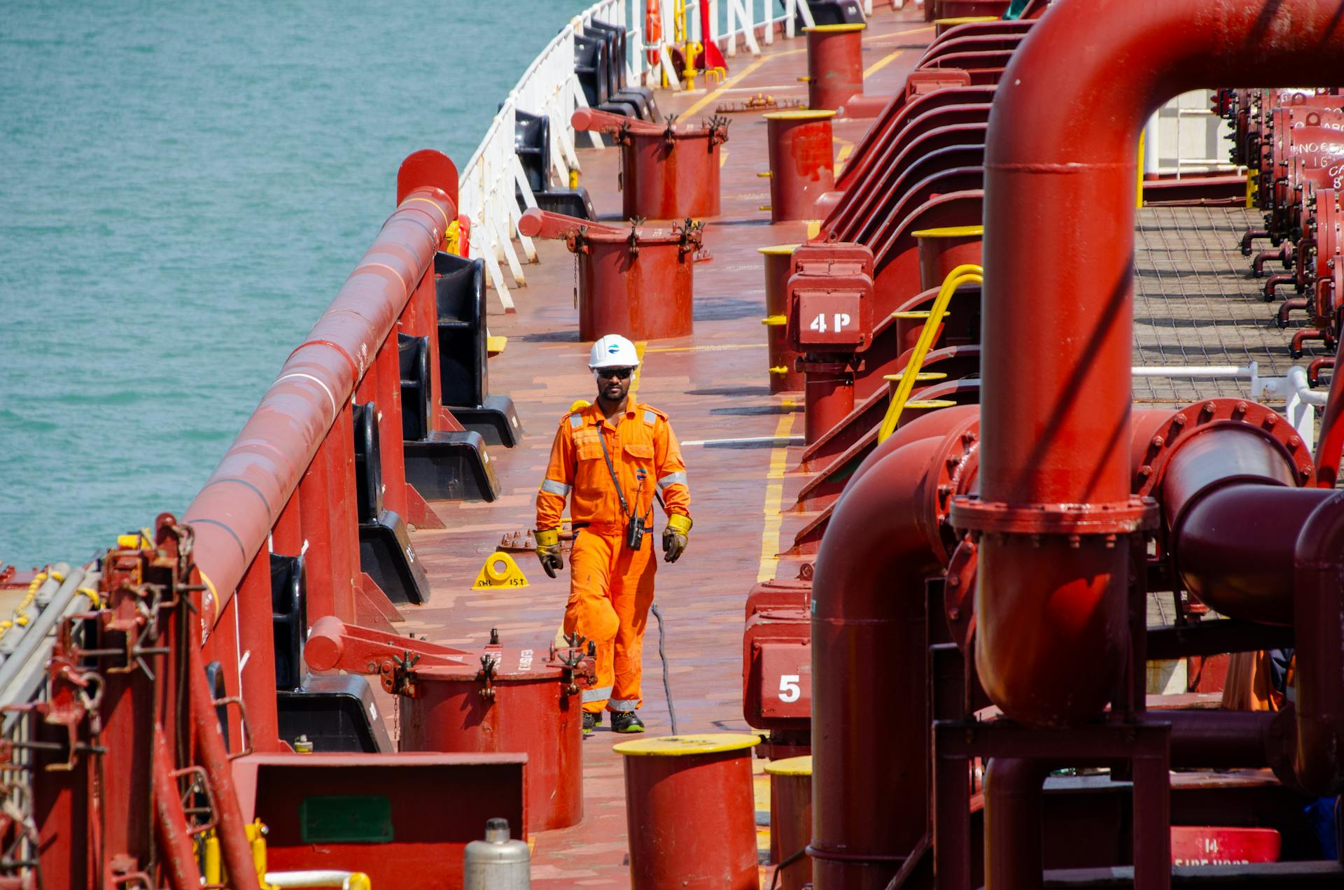 Oil tanker worker in safety gear performing inspection on deck. Vibrant and professional setting.