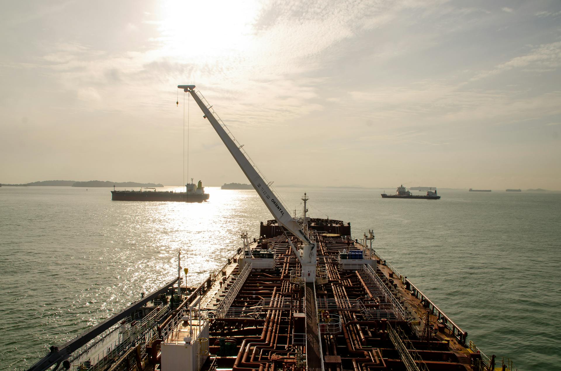 A cargo ship sails into the sunlit sea, passing other vessels in a serene maritime view.