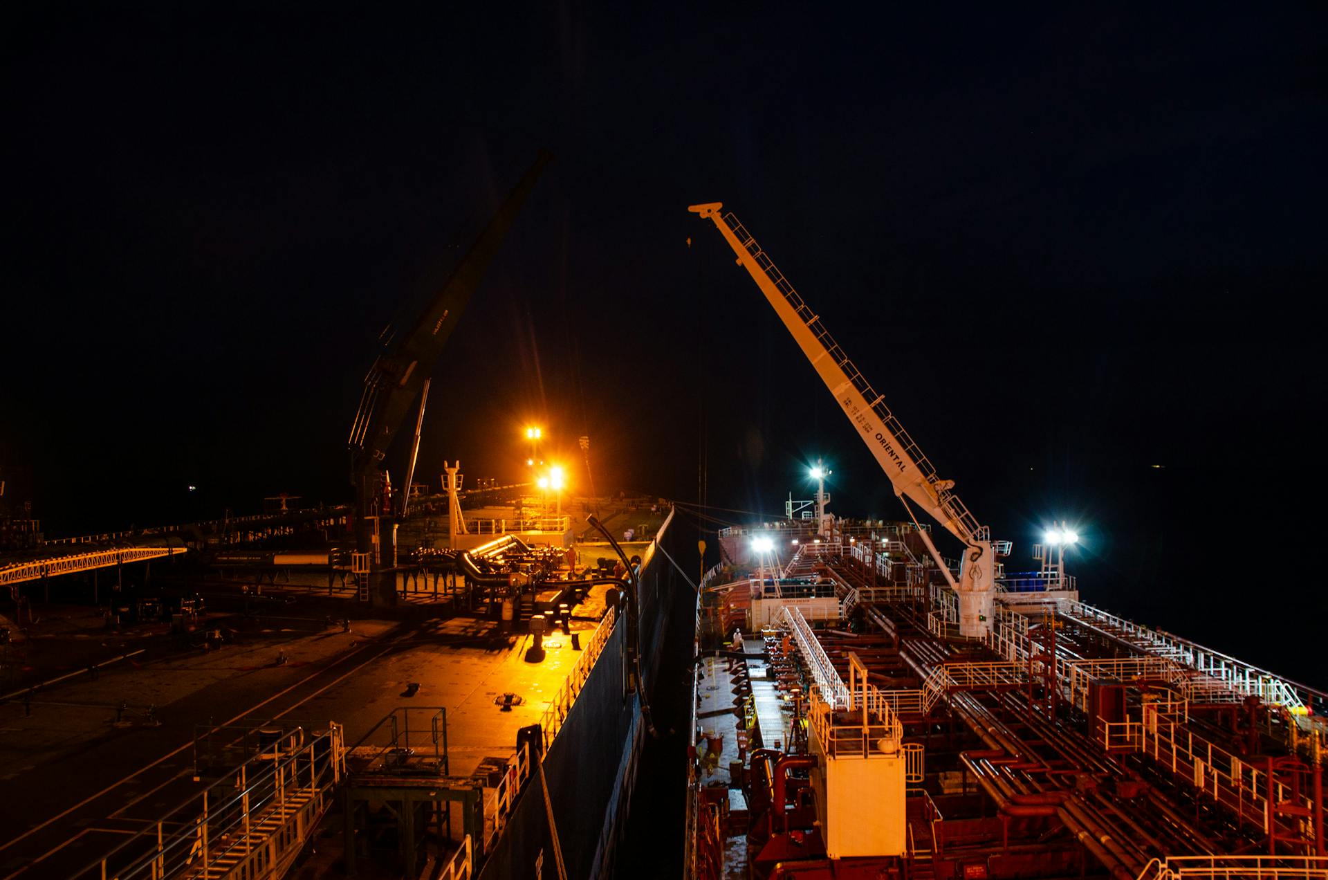 Illuminated ship deck with cranes operating at night, showcasing industrial maritime activities.