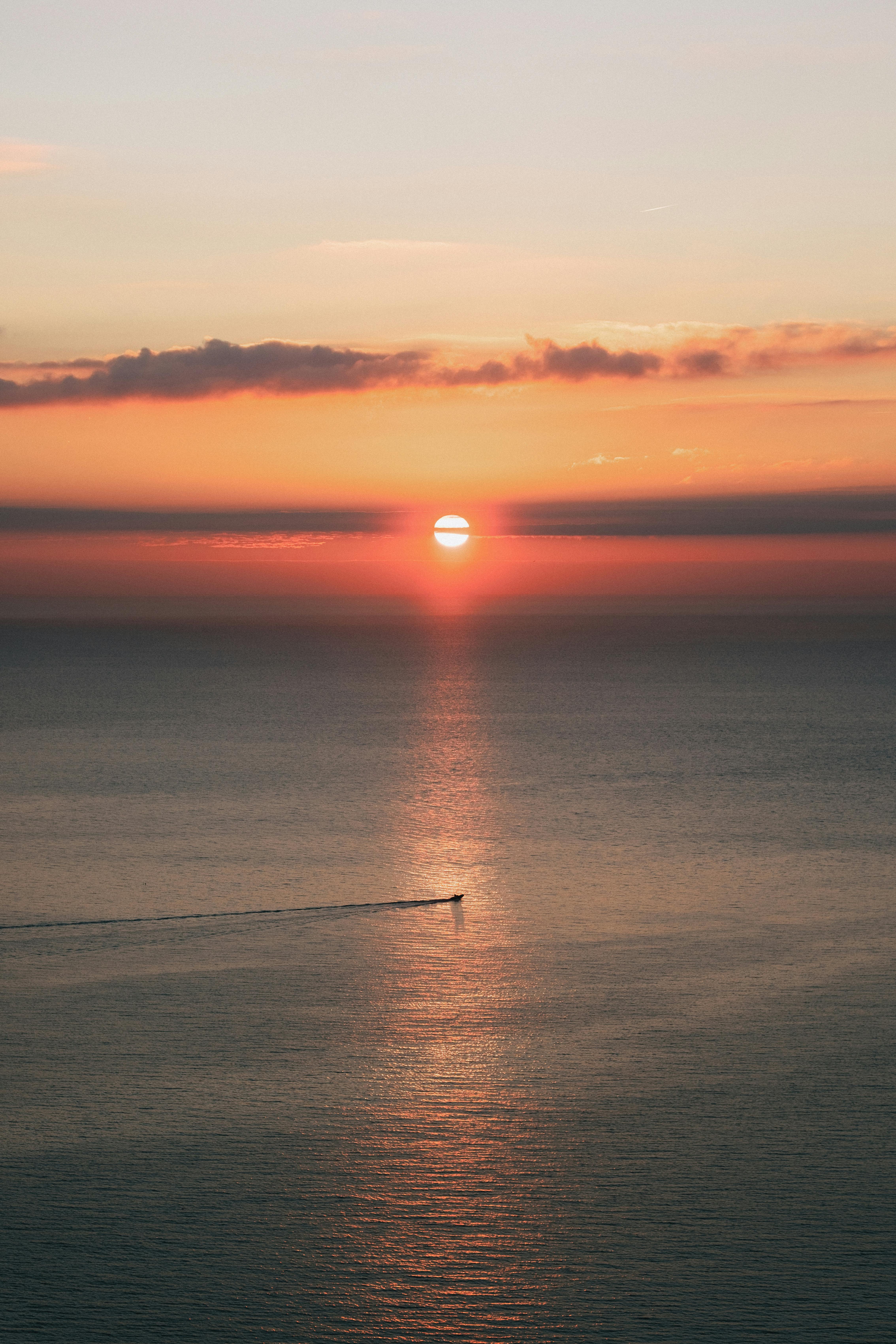 宁静的日落映照在海洋与一艘单船，以及充满活力的天空上