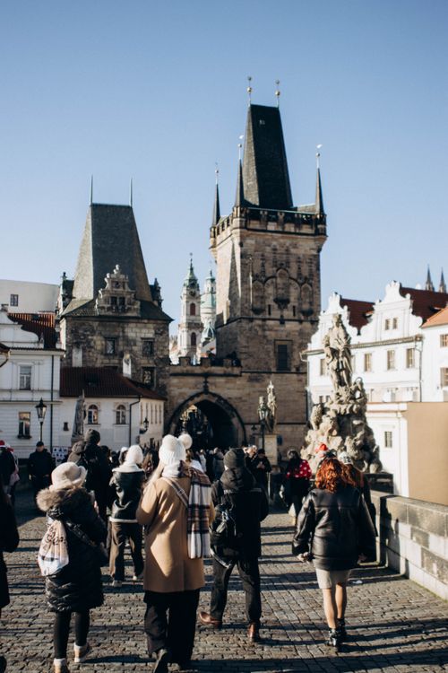 Free Tourists walk on the Charles Bridge in Prague, showcasing its Gothic towers under a clear sky. Stock Photo