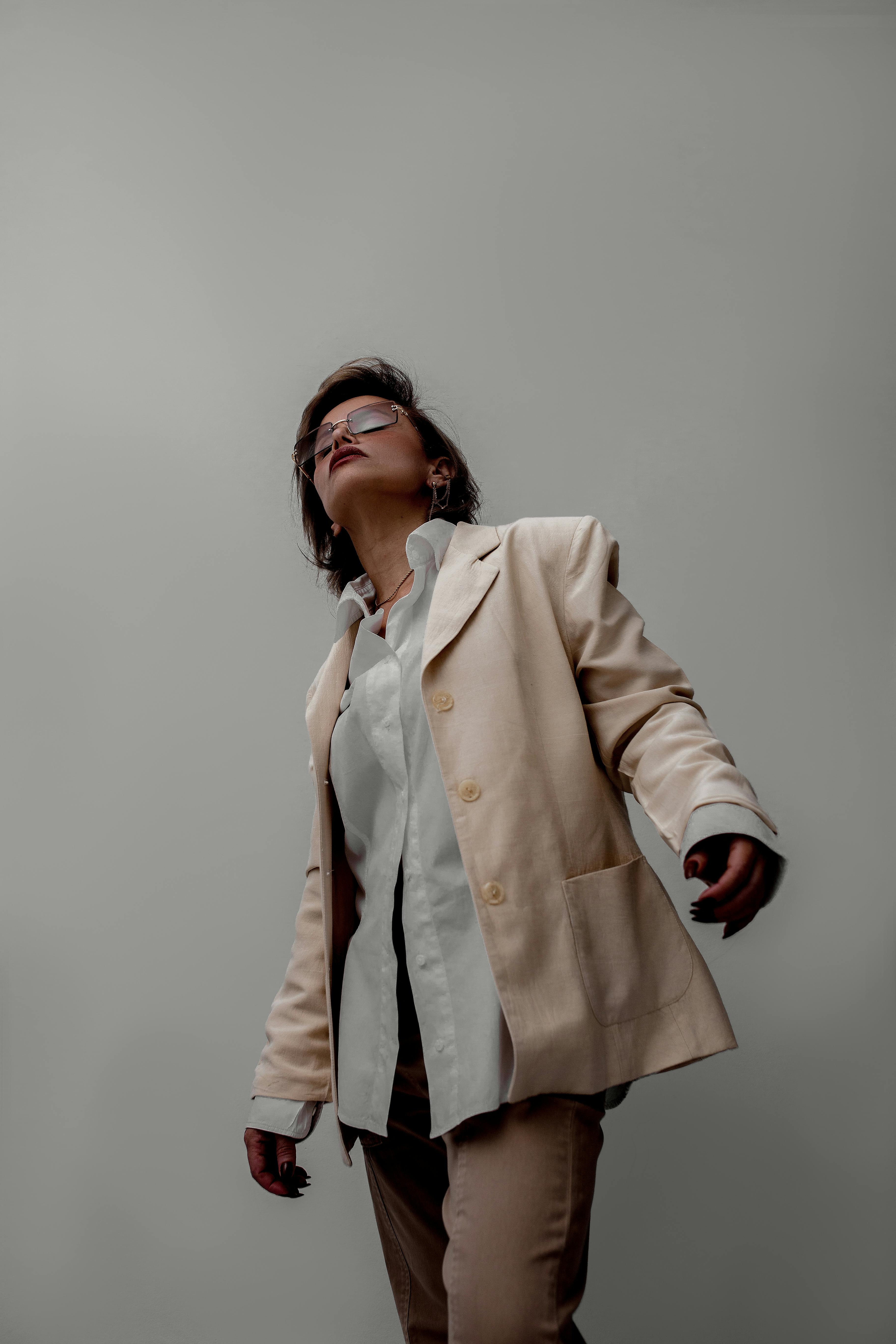 De franc Dona elegant amb un vestit beix i ulleres de sol, posant sobre un teló de fons neutre. Foto d'estoc