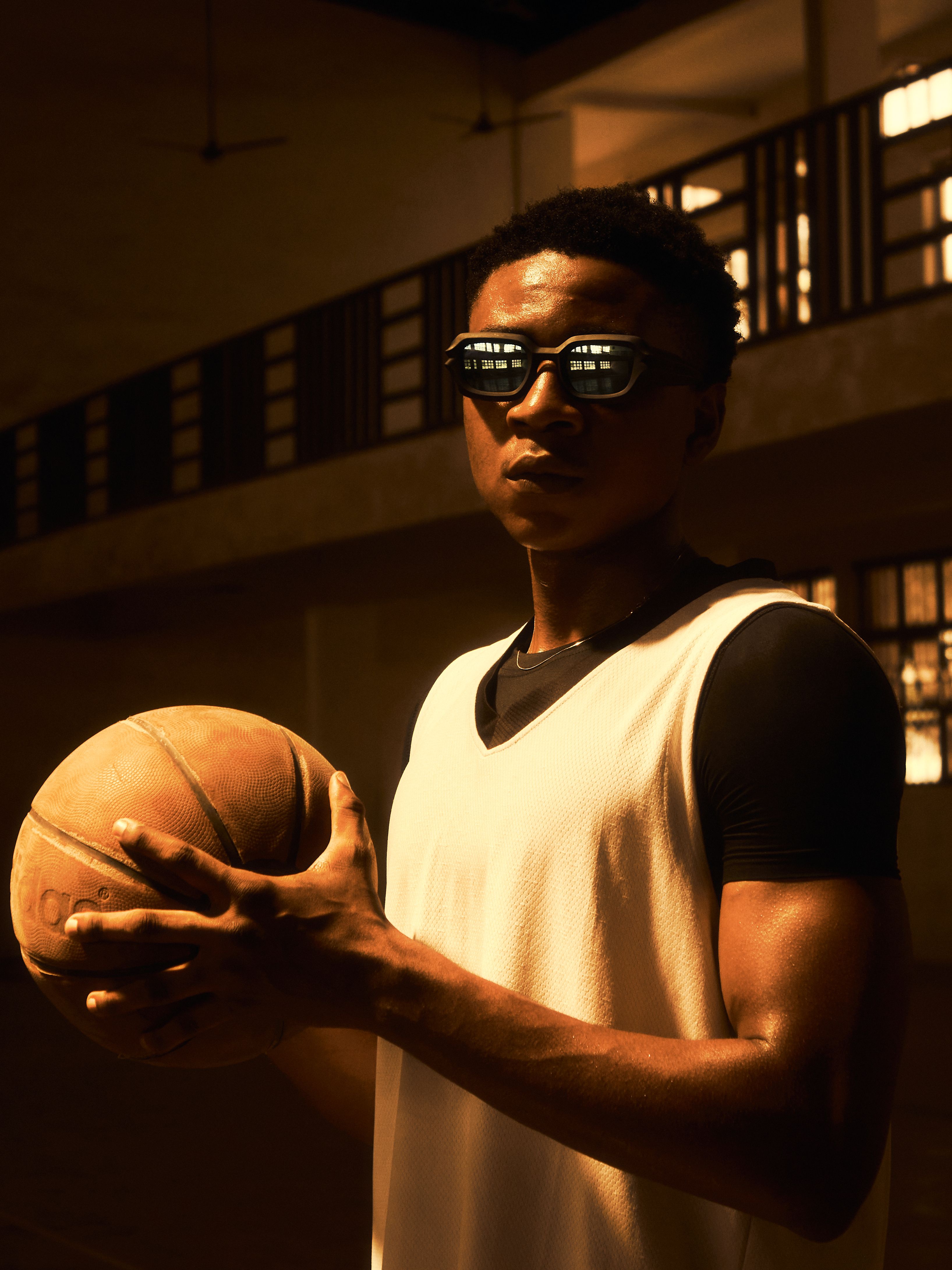 Confident young basketball player stands indoors with sunglasses, preparing for the game.